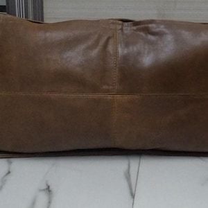 Puede incluir: Una almohada de cuero marrón con forma rectangular y un diseño cosido.