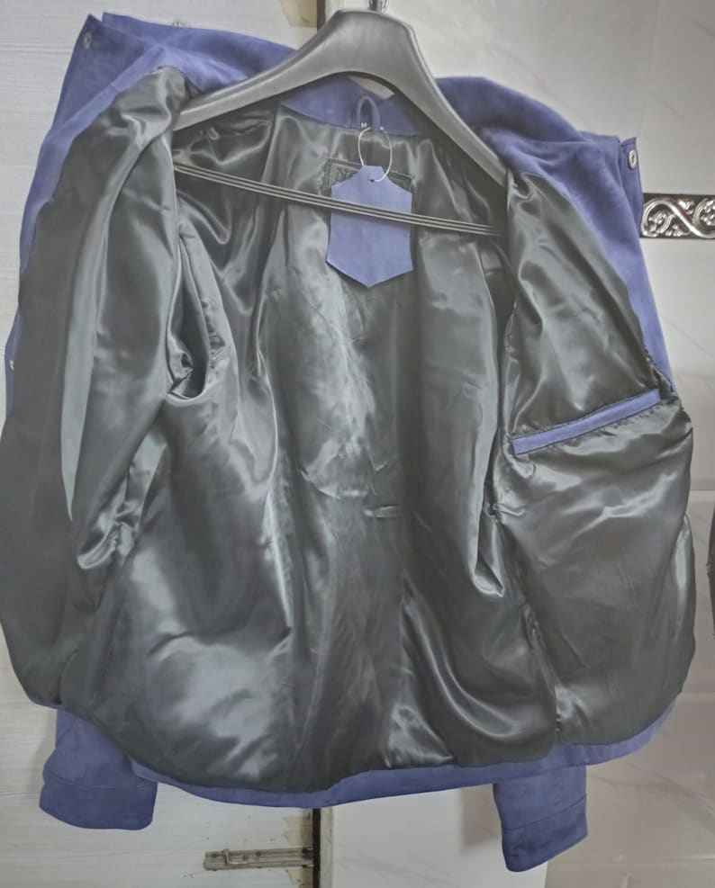 May include: A blue suede jacket with a black satin lining. The jacket has a zip closure and a pocket on the inside.