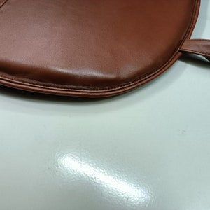May include: A brown leather chair cushion with a stitched edge and a loop handle.