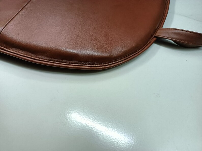 May include: A brown leather chair cushion with a stitched edge and a loop handle.