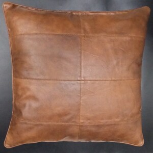 May include: A brown leather pillow with a square design. The pillow is made of multiple pieces of leather that are sewn together.