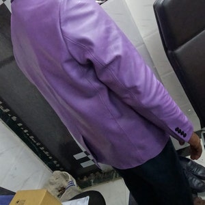 May include: A purple leather blazer with a buttoned cuff. The blazer is worn by a person standing in a room with a chair and a box.