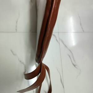 May include: Brown leather chair cushion with two brown leather ties. The cushion is tied at the bottom.