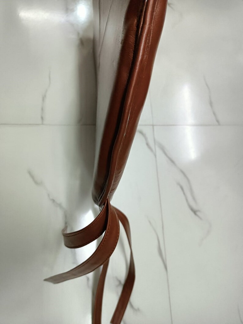 May include: Brown leather chair cushion with two brown leather ties. The cushion is tied at the bottom.