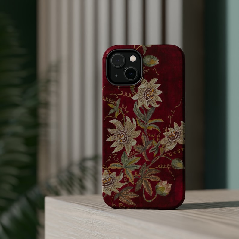May include: A red phone case with a floral design featuring white flowers and green leaves. The case has a camera cutout and a black border.