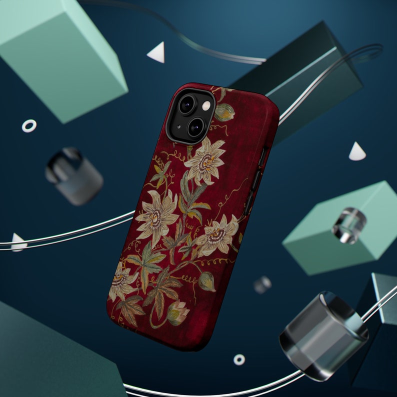 May include: A red phone case with a floral design featuring white flowers and green leaves. The case has a raised camera bump with three lenses.