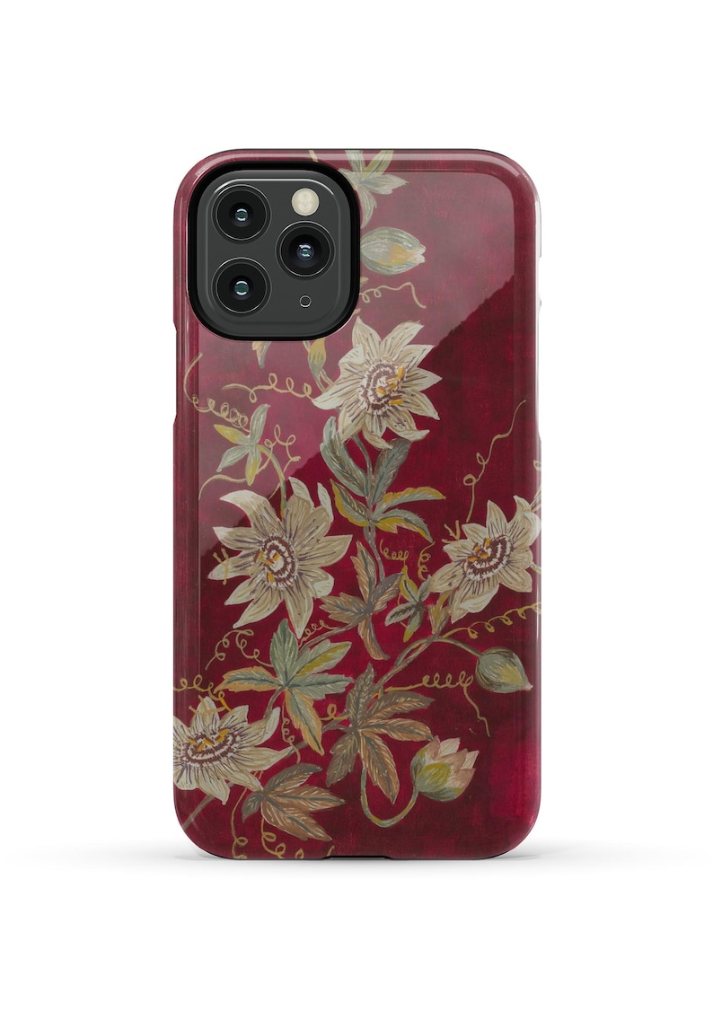 May include: A red phone case with a floral design featuring white flowers and green leaves. The flowers have a yellow center and are arranged in a pattern that resembles a vine.