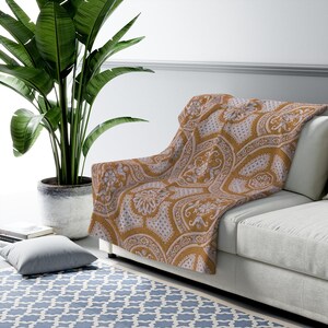 May include: A mustard yellow throw blanket with a white paisley pattern. The blanket is draped over a light brown sofa.