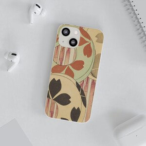 May include: A phone case with a Japanese-inspired design. The case features a cream-colored background with circular patterns in shades of brown, red, and green. Vertical bamboo-like stripes are also visible. The case is shown with white wireless earbuds.