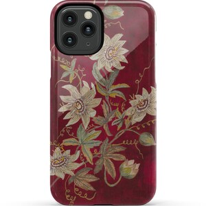 May include: A red phone case with a floral design featuring white flowers and green leaves. The case has a glossy finish.