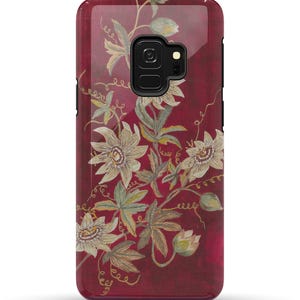 May include: A burgundy phone case with a floral design featuring white flowers and green leaves. The case has a cutout for the phone's camera.