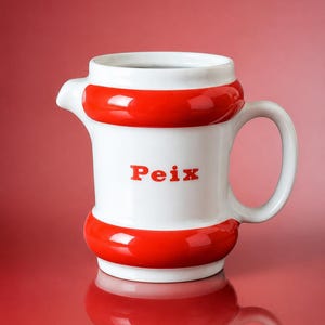 May include: A white ceramic pitcher with a glossy finish, featuring two thick, horizontal red bands encircling the top and bottom. The word Peix is printed in red letters on the center of the body. It has a curved handle and a small pouring spout.
