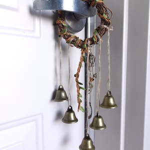 May include: A brown twig wreath with green leaves and small gold bells hanging from it. The wreath is attached to a white door with a silver door handle.