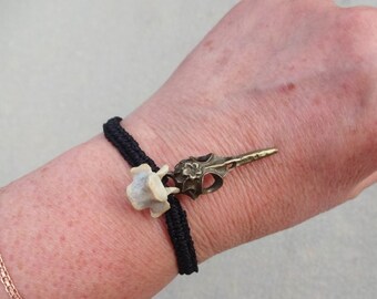 May include: A black elastic bracelet with a gold bird skull charm and a white bone charm.