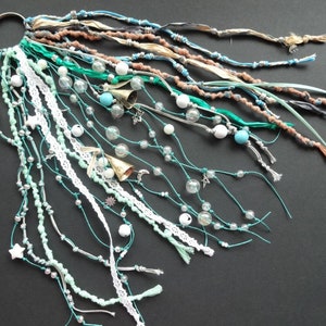 May include: A teal and white beaded and string hair wrap with bells, stars, and moon charms.