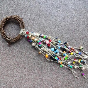 May include: A twig wreath with a long, colourful beaded tassel hanging from it. The beads are a mix of blue, green, red, yellow, and white.