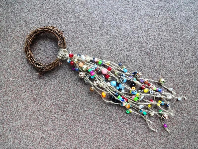 May include: A twig wreath with a long, colourful beaded tassel hanging from it. The beads are a mix of blue, green, red, yellow, and white.