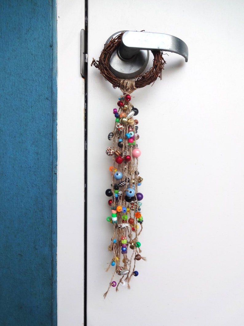 May include: A door handle with a wreath of twigs and a long strand of colourful beads hanging from it.
