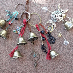 May include: A collection of six silver bells with red, blue, and black tassels hanging from a brown leather cord. The bells are decorated with various charms, including a dragon, a star, and a Celtic knot.
