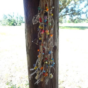May include: A colourful beaded and bell wind chime with a leaf charm hanging from a wooden post. The wind chime is made of natural fibres and features a variety of beads in different colours and shapes.
