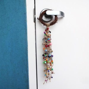 May include: A colourful beaded door hanger with a twig wreath and a long tassel of beads in various colours, including red, blue, green, and yellow.
