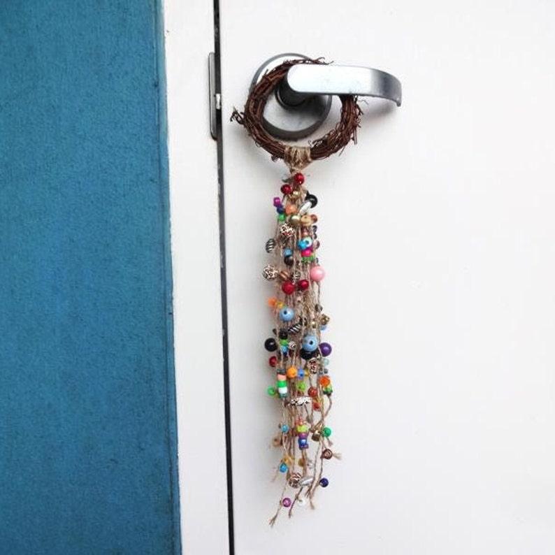 May include: A colourful beaded door hanger with a twig wreath and a long tassel of beads in various colours, including red, blue, green, and yellow.
