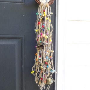 May include: A colourful door hanging with beads, bells, and tassels. The hanging is made of natural fibres and has a rustic, bohemian style.