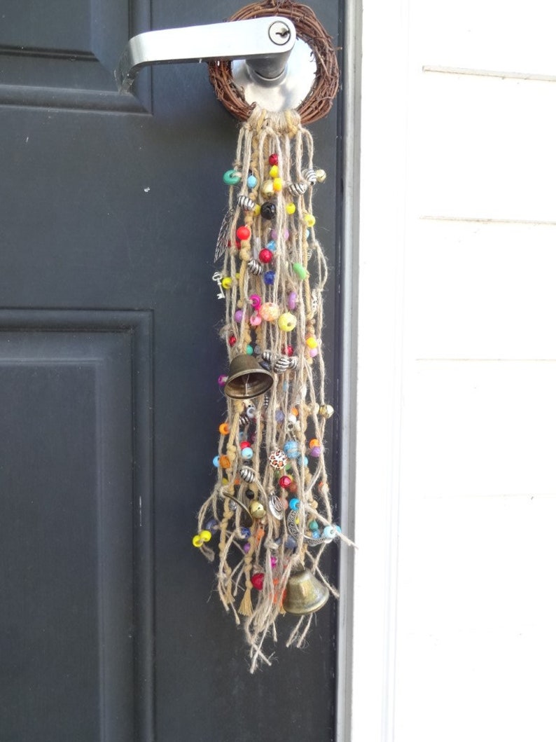 May include: A colourful door hanging with beads, bells, and tassels. The hanging is made of natural fibres and has a rustic, bohemian style.