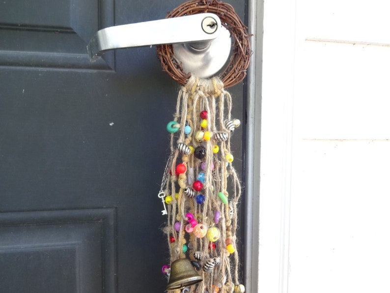 May include: A door with a wreath made of twigs and a door handle with a long strand of colourful beads and a small bell hanging from it.