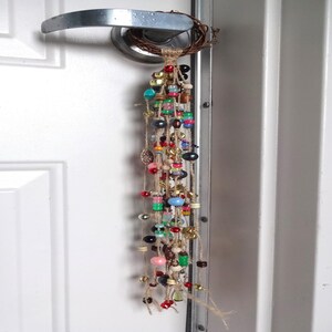 May include: A colourful beaded door hanging with a woven twig base. The beads are strung on twine and include various colours, shapes, and sizes.