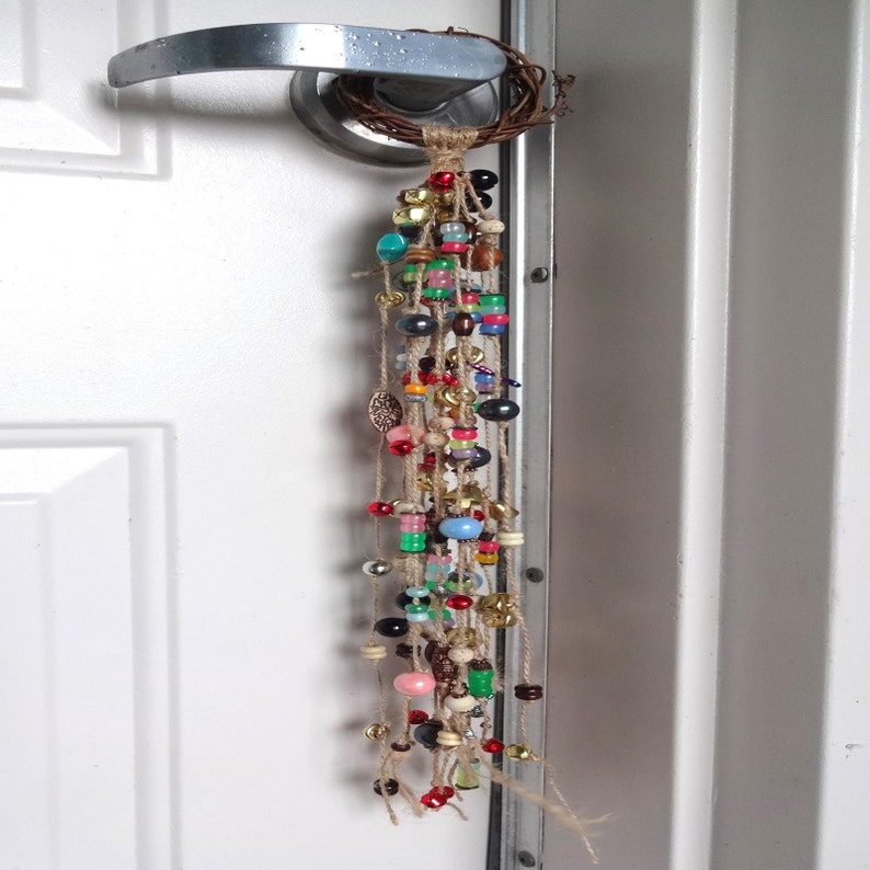 May include: A colourful beaded door hanging with a woven twig base. The beads are strung on twine and include various colours, shapes, and sizes.