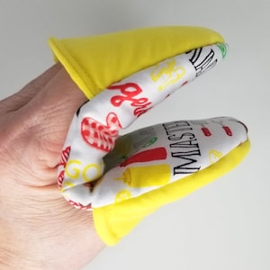 May include: Yellow and white oven mitt with a barbecue theme. The mitt has a yellow exterior and a white interior with red, yellow, and black graphics of grilling tools and the word "MASTER".