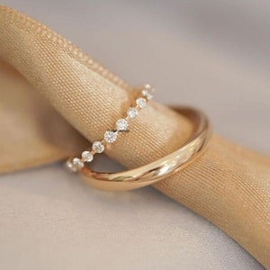 Può includere: Due anelli d'oro, uno con una fila di piccoli diamanti, sono esposti su uno sfondo di tessuto beige.
