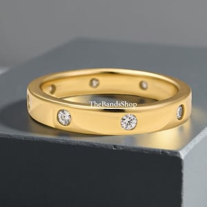 Könnte beinhalten: Ein goldfarbener Ring mit mehreren kleinen, klaren Edelsteinen, die in das Band eingesetzt sind. Der Ring hat eine glatte, polierte Oberfläche. Der Text "TheBandsShop" ist auf dem Band sichtbar.