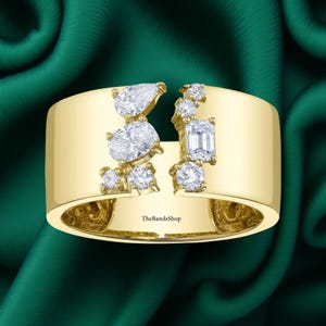 Puede incluir: Un anillo de banda ancha de oro con diseño abierto y un grupo de diamantes transparentes de varias formas a cada lado. Los diamantes incluyen cortes de pera, óvalo, redondo y esmeralda. El interior de la banda tiene grabado el texto TheBandsShop.