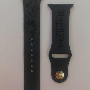 Può includere: Cinturino per Apple Watch nero con personaggi anime incisi e la scritta "DEATH NOTE". Il cinturino ha una chiusura a fibbia e fori di regolazione. Il design è un omaggio alla popolare serie anime.