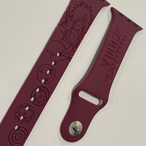 Può includere: Cinturino per Apple Watch color bordeaux con un personaggio anime e simboli incisi. Il cinturino include il testo "MADARA UCHIHA" ed è progettato per uno smartwatch. Il cinturino è realizzato in materiale flessibile.