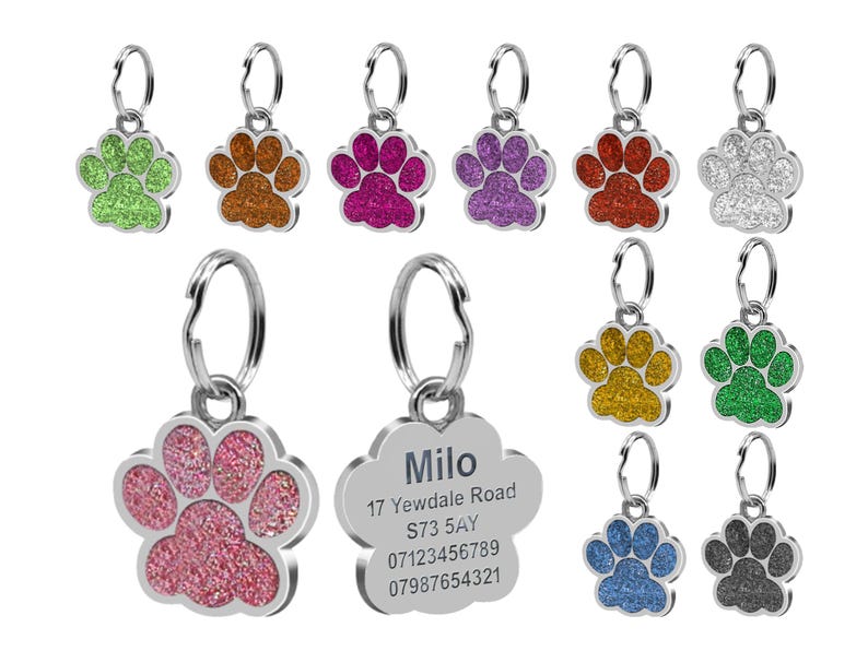 May include: A selection of silver paw print dog tags with glitter accents in various colours, including green, orange, pink, purple, red, silver, gold, blue, and black. One tag features the name "Milo" and contact details.