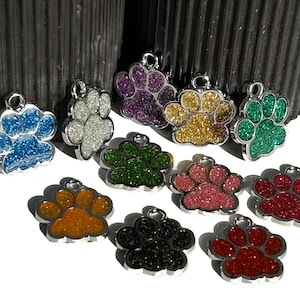 May include: Ten silver paw print charms with different colored glitter finishes. The charms are in a variety of colors including blue, white, purple, gold, green, pink, orange, black, and red.