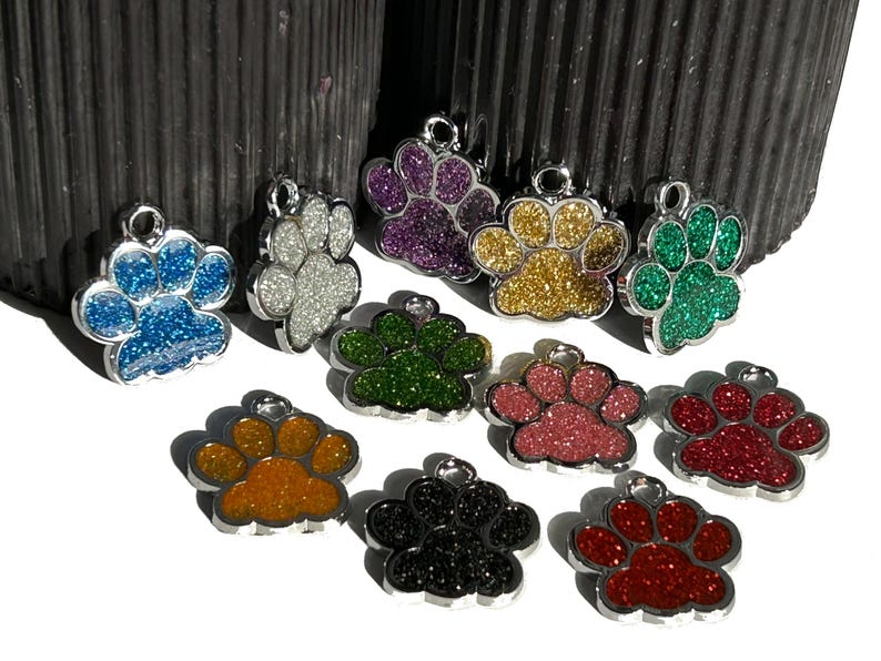 May include: Ten silver paw print charms with different colored glitter finishes. The charms are in a variety of colors including blue, white, purple, gold, green, pink, orange, black, and red.