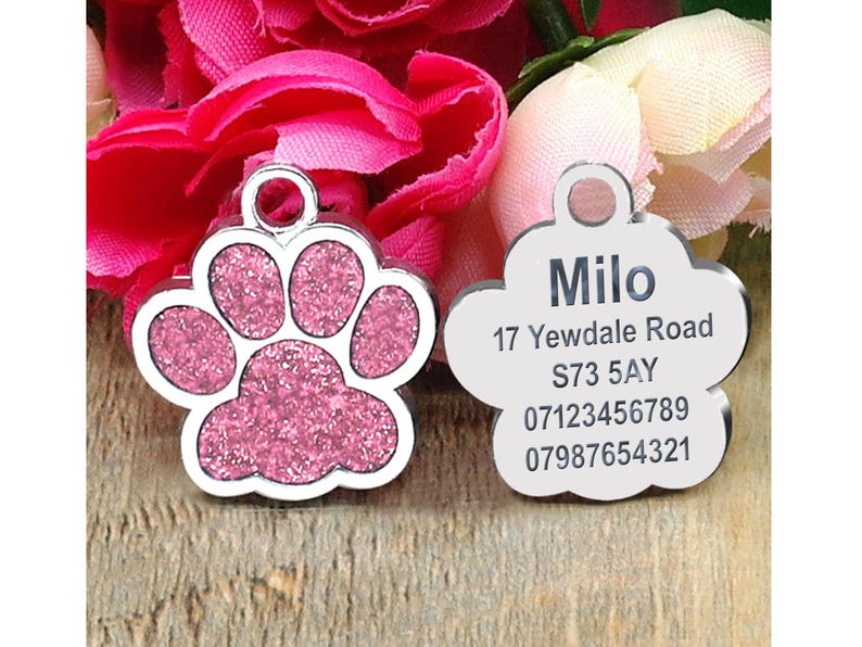 May include: Two silver dog tags, one shaped like a paw print with pink glitter and the other a cloud shape. The paw print tag is blank. The cloud tag has the name "Milo", address "17 Yewdale Road", postcode "S73 5AY", and phone numbers "07123456789" and "07987654321".