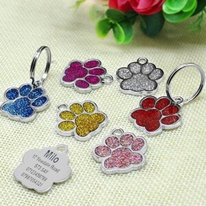 May include: Six silver paw print dog tags with glitter accents in blue, red, pink, gold, silver, and purple. The tags are attached to key rings. One tag has a silver engraved tag with the text "Milo, 17 Yewdale Road, ST3 5AY, 07121456789, 07981654321".
