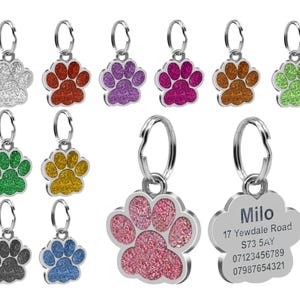 May include: Assortment of colorful glitter paw print dog tags with a silver metal ring. One tag has the name "Milo" and contact information.