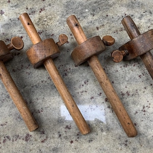 May include: Four wooden marking gauges arranged in a row. Each tool consists of a long cylindrical stem, a sliding wooden block, and a small metal thumbscrew used to secure the block in place along the stem for measuring and marking wood.