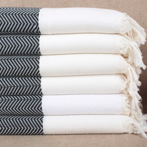 May include: A stack of six white towels with black and white chevron patterned borders. The towels have fringe edges and are folded neatly.