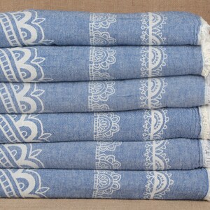May include: A stack of six blue and white patterned towels with fringed edges. The towels are folded and stacked on a brown surface.
