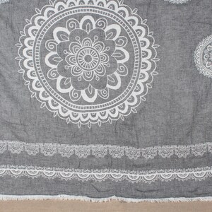 Puede incluir: Manta de algodón gris con un diseño de mandala blanco. La manta tiene un borde de flecos.