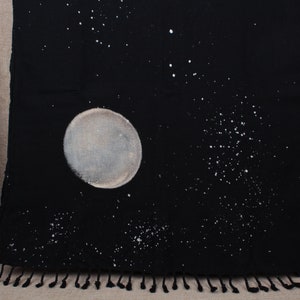 May include: Black cotton fabric with a white moon and stars design. The fabric has a fringe border.