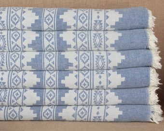 May include: A stack of six blue and white patterned towels with fringe edges. The towels are folded and stacked on a brown surface.
