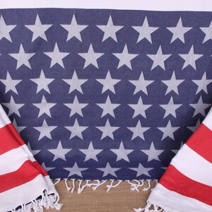 Puede incluir: Dos banderas americanas, una azul con estrellas blancas y otra roja y blanca, están drapeadas sobre una superficie marrón. La bandera azul tiene un borde con flecos.